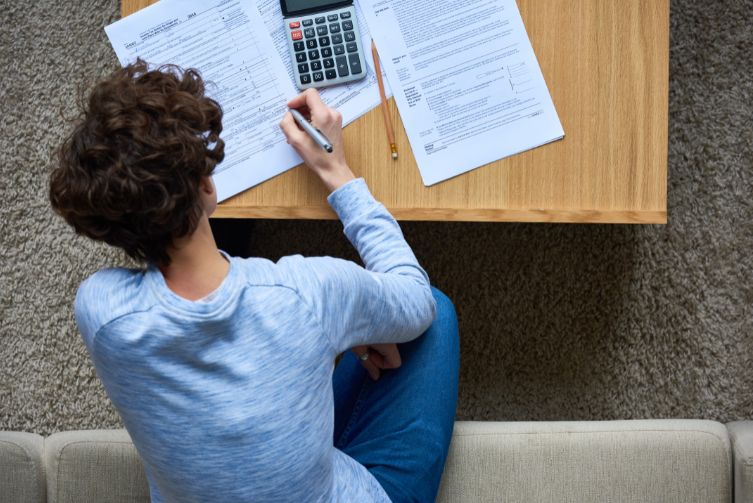 A person sits with tax papers and a calculator around them