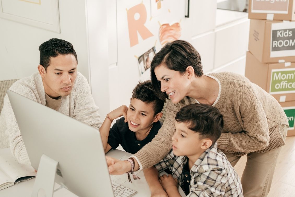 A father and mother gather around their two children who are sitting in front of a desktop computer.