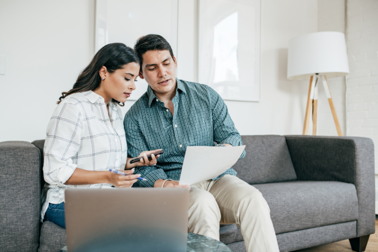 A woman and a man sit on a couch while going over a statement.