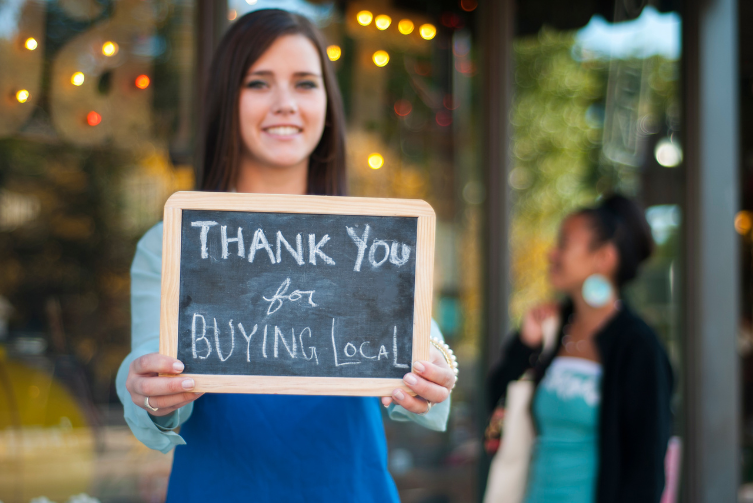 A young woman holds a sign that says, "Thank you for buying local"