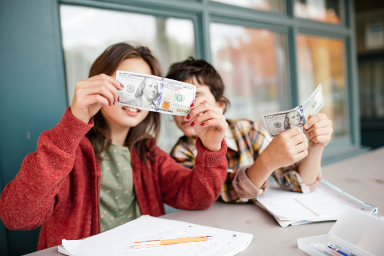 A girl and a boy each hold a one hundred dollar bill