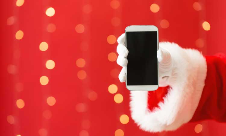 Santa's hand holding a cell phone with twinkling lights in the back